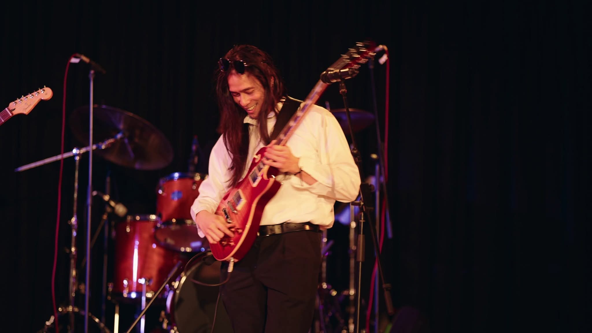 Ming Yao playing a red electric guitar on stage, smiling mid-song